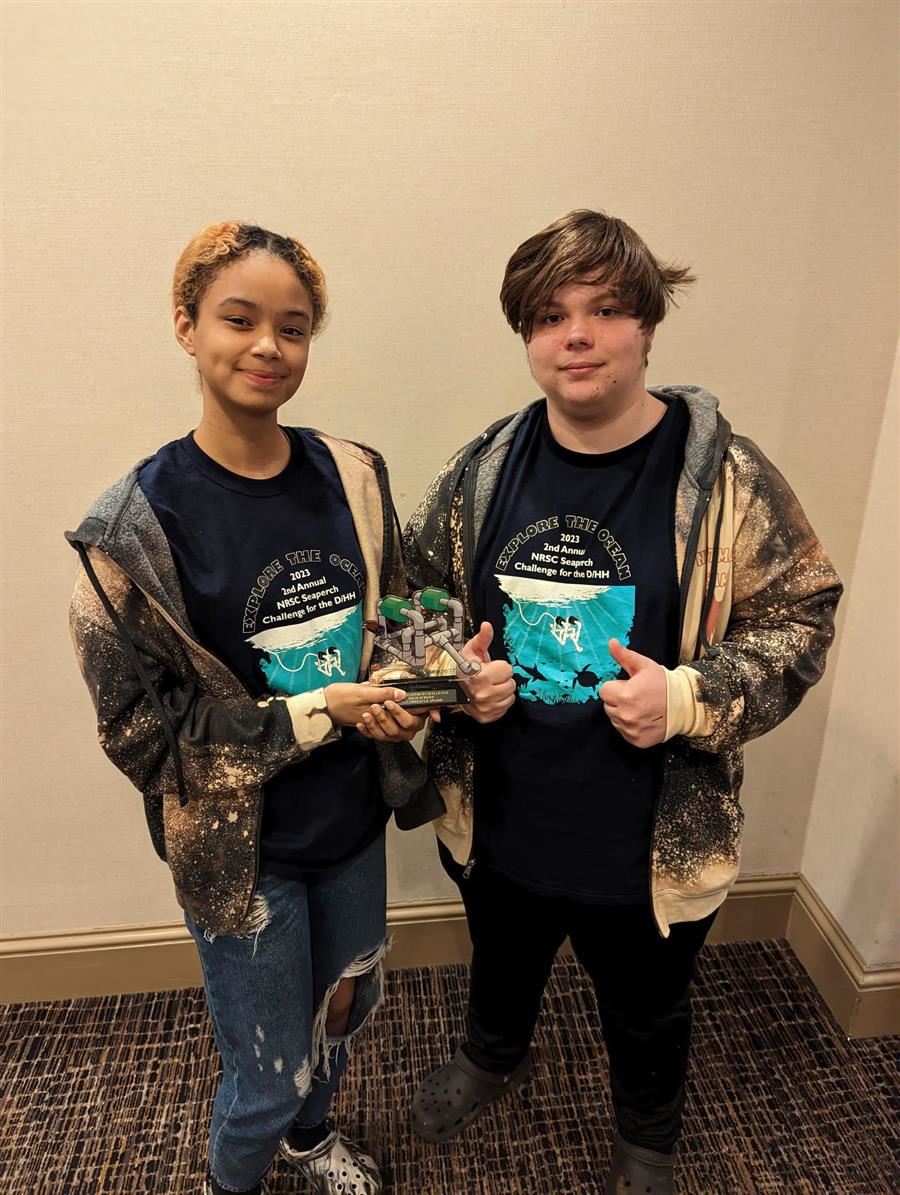  Melika and Brayden hold their trophy. Melika smiles to camera while Brayden gives a thumbs up.